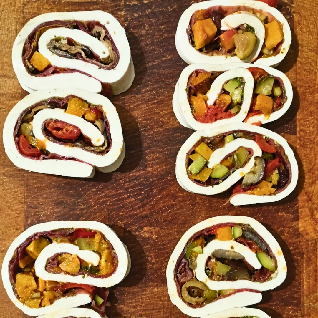 Rotolini di mozzarella farcita con pesto, bresaola e verdure miste fresche su tagliere di legno